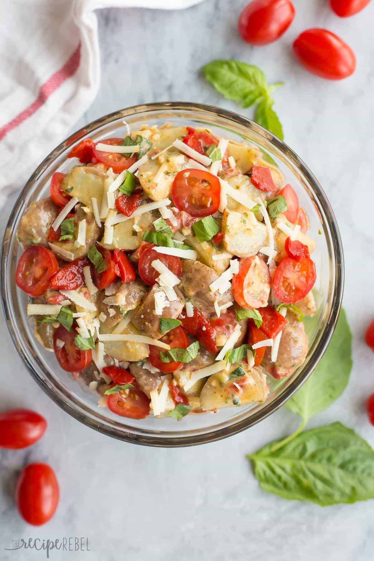overhead image of italian potato salad in clear bowl with cherry tomatoes and fresh basil