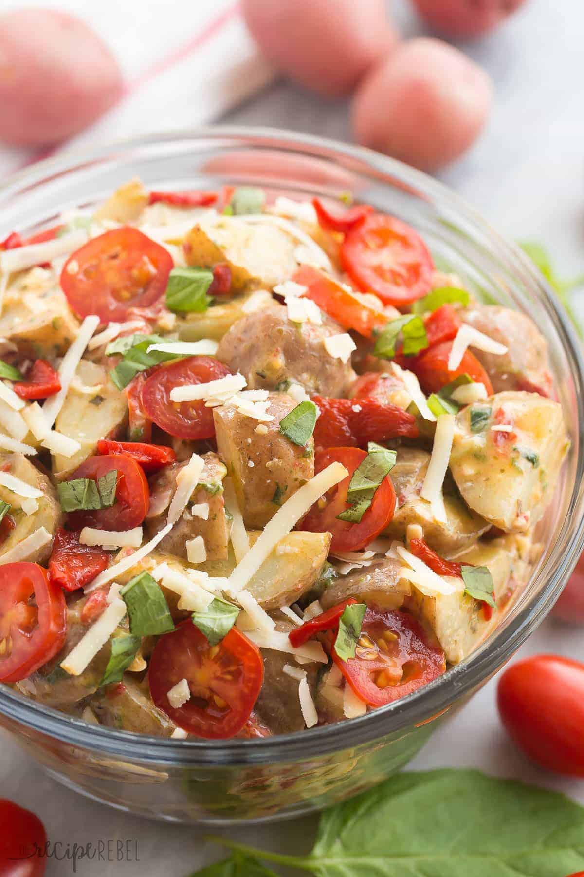 close up of italian potato salad in glass bowl with shredded cheese and tomatoes
