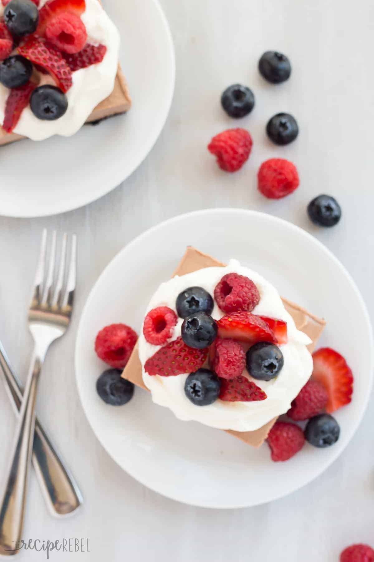 overhead image of nutella cheesecake bars on white plate with whipped cream and fresh berries
