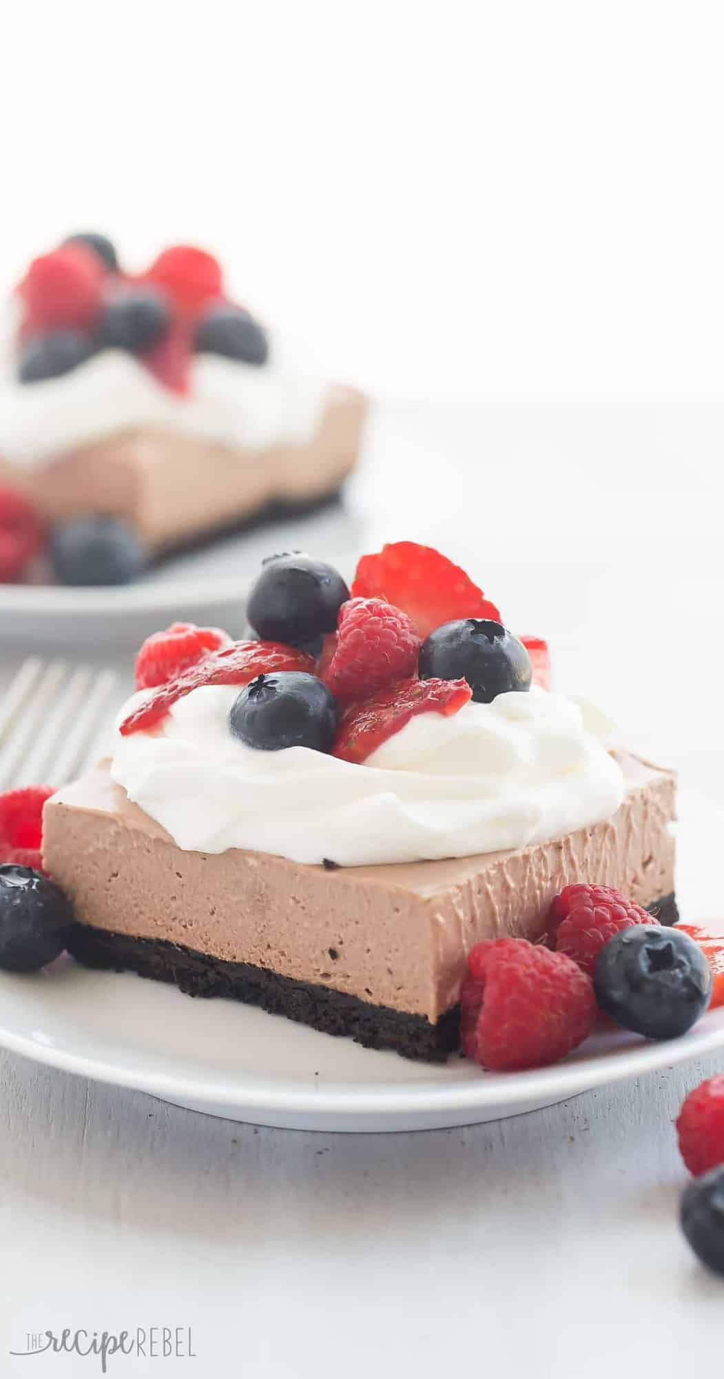 close up image of nutella cheesecake bars on white plate with whipped cream and fresh berries