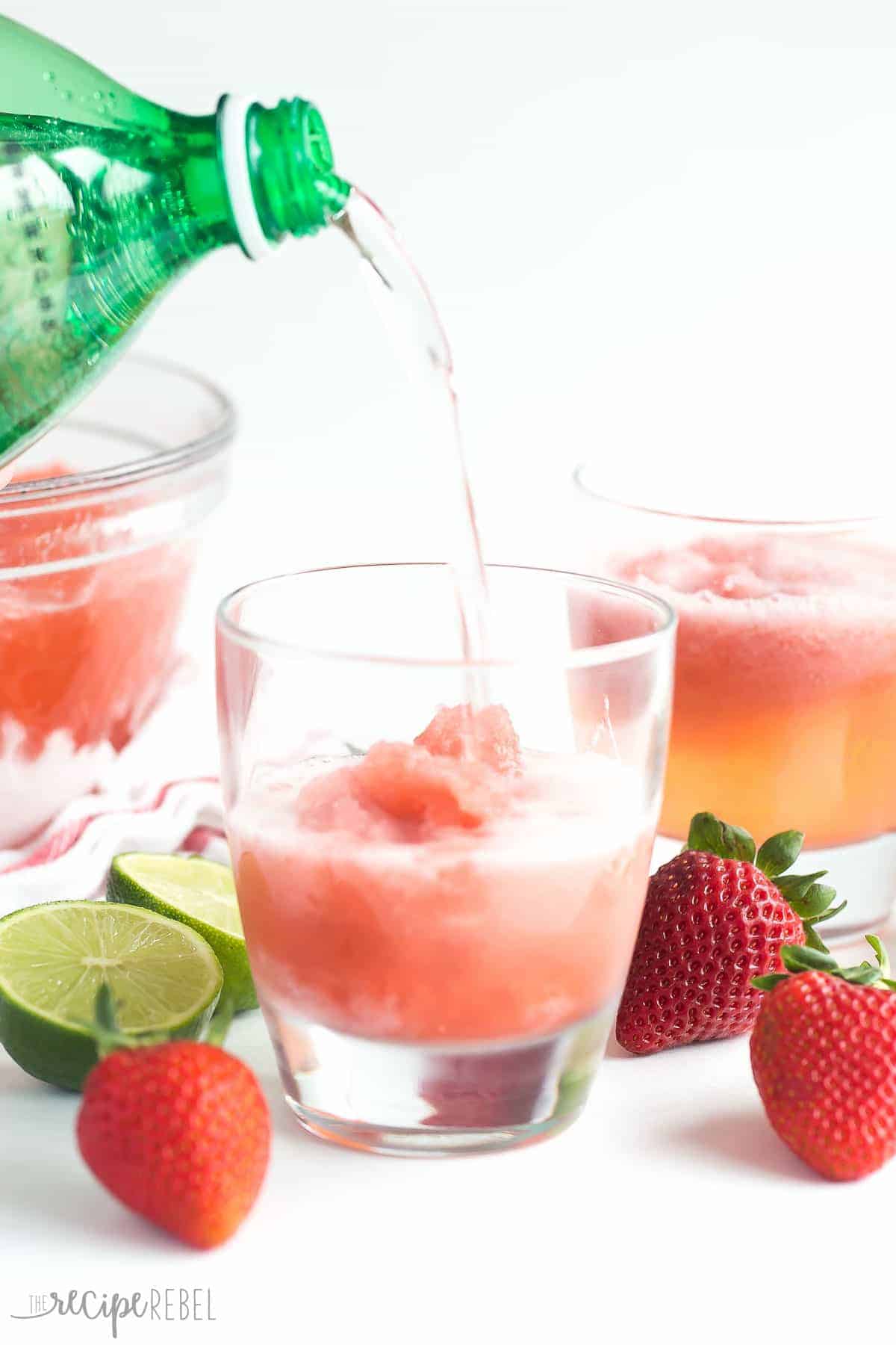 berry lime slush in glasses with lime halves and strawberries and pop being poured in
