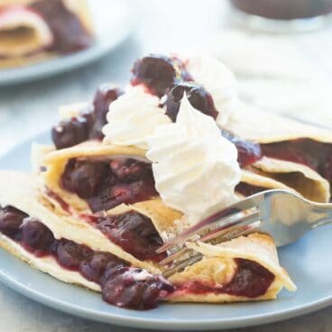 These Cherry Cheesecake Crepes are filled with sweetened cream cheese and homemade cherry pie filling, then topped with whipped cream and extra cherries! They are perfect for dessert or a special breakfast or brunch!