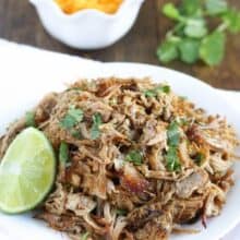 white plate filled with crockpot pork carnitas and lime wedge on side