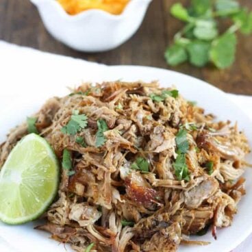 white plate filled with crockpot pork carnitas and lime wedge on side