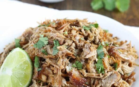 white plate filled with crockpot pork carnitas and lime wedge on side