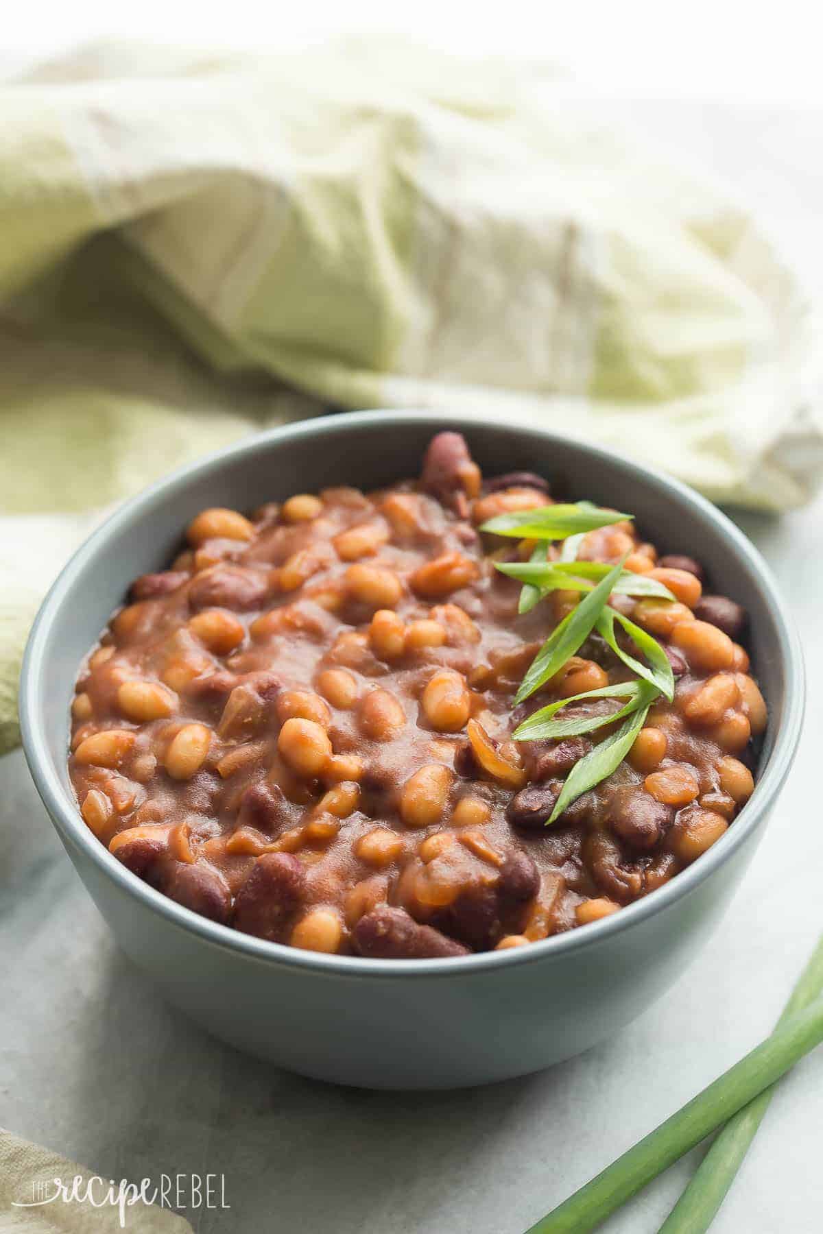 bowl of slow cooker baked beans with green onions on top and green towel in the background