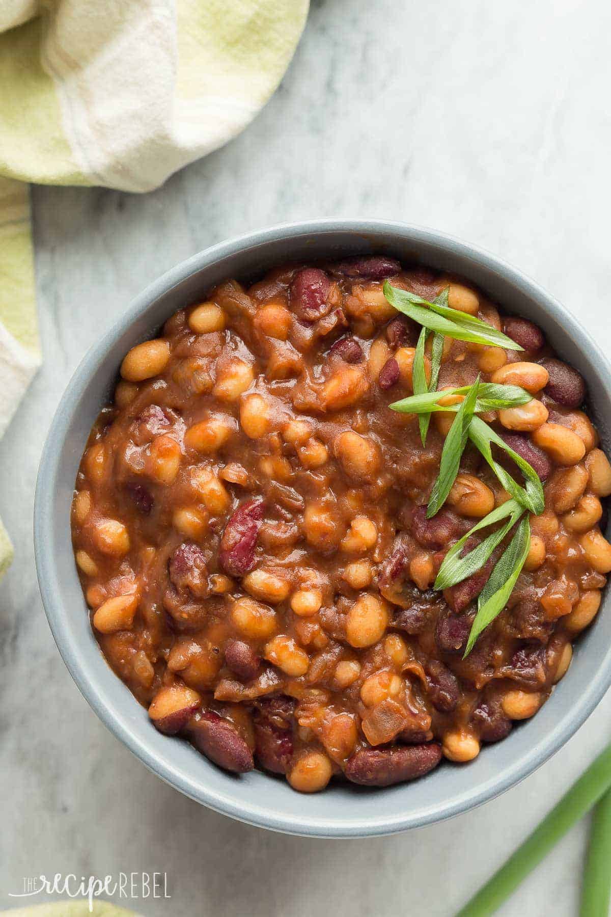 overhead image of grey bowl of slow cooker baked beans with sliced green onions on top