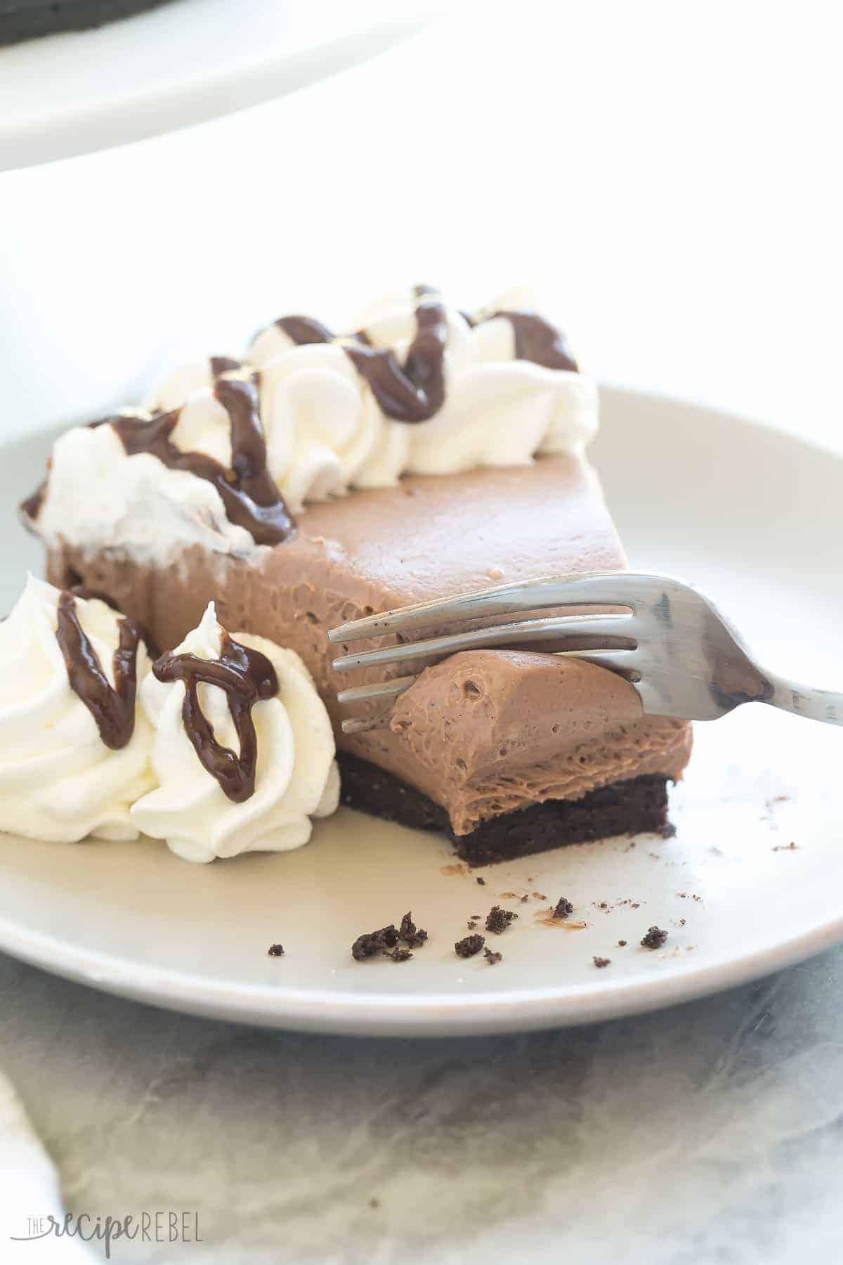 piece of no bake brownie batter cheesecake on grey plate with whipped cream and brownie batter drizzle