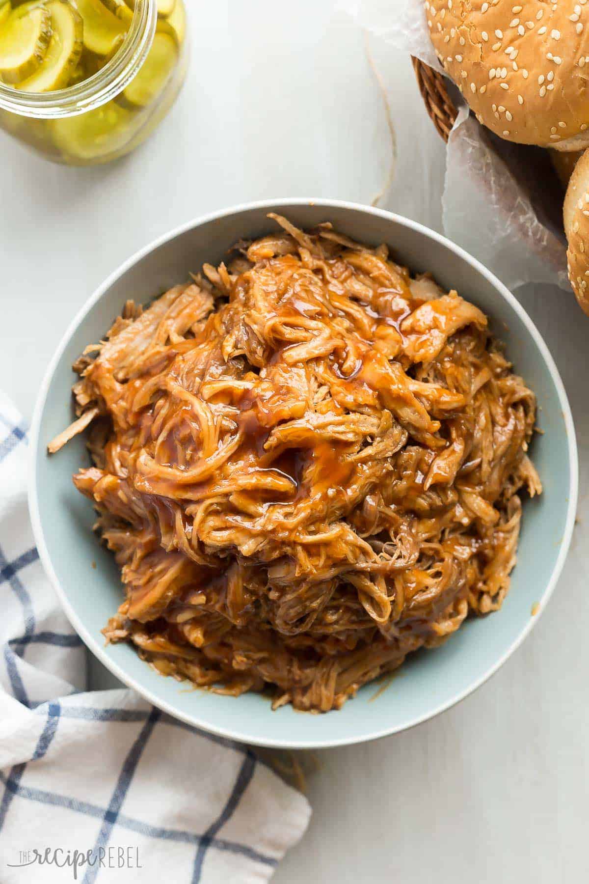 overhead image of slow cooker pineapple brown sugar pulled pork in blue bowl with buns on the side