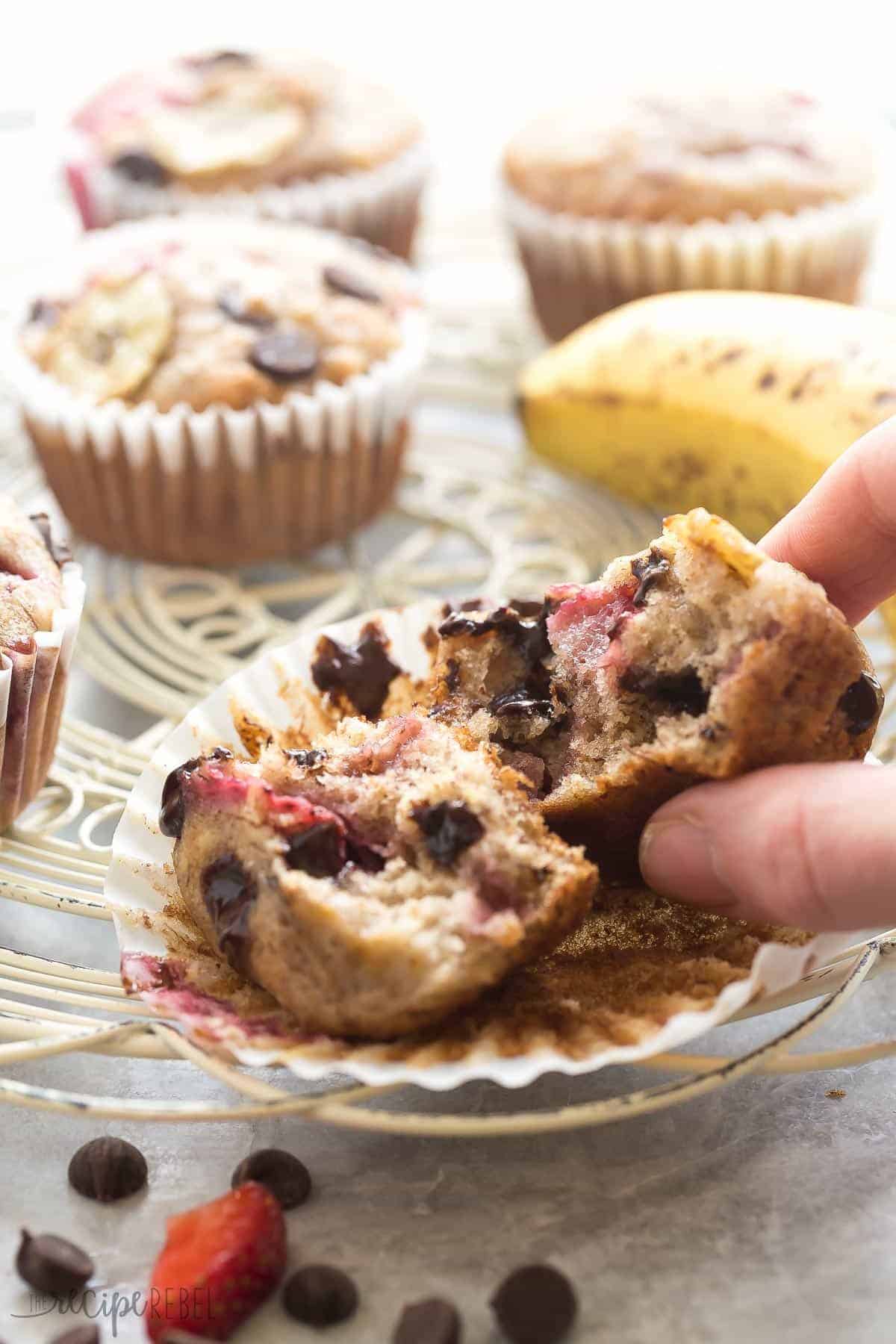 strawberry banana chocolate chip muffin broken in half with hand grabbing half