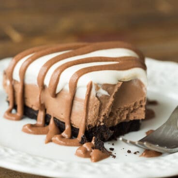 no bake brownie batter piece on white plate with whipped cream and brownie batter drizzle