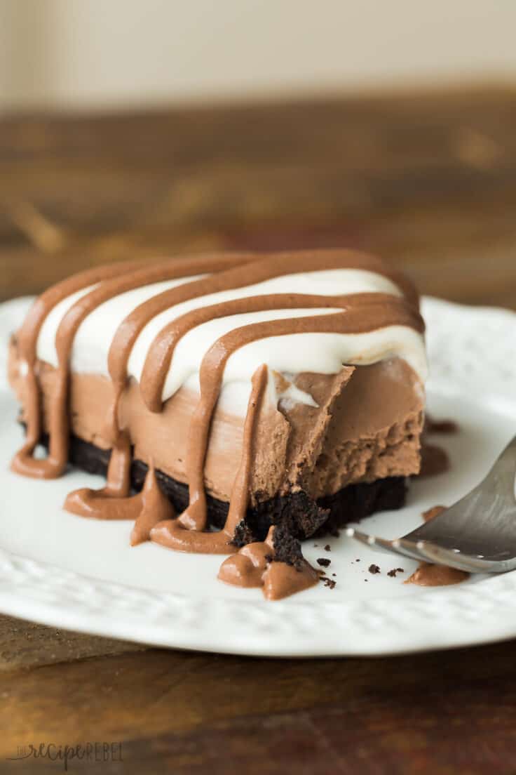 This No Bake Brownie Batter Cheesecake is the cheesecake for chocolate lovers! It's rich and fudgy with no oven required! no bake brownie batter piece on white plate with whipped cream and brownie batter drizzle