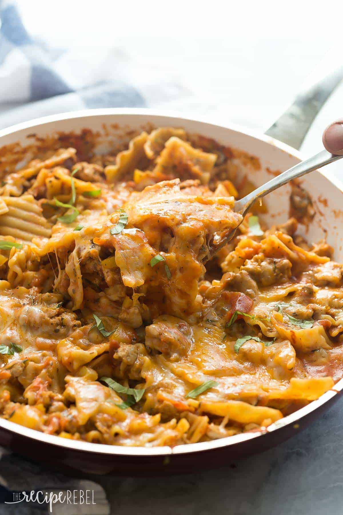 skillet lasagna in white pan with metal scoop pulling up some noodles