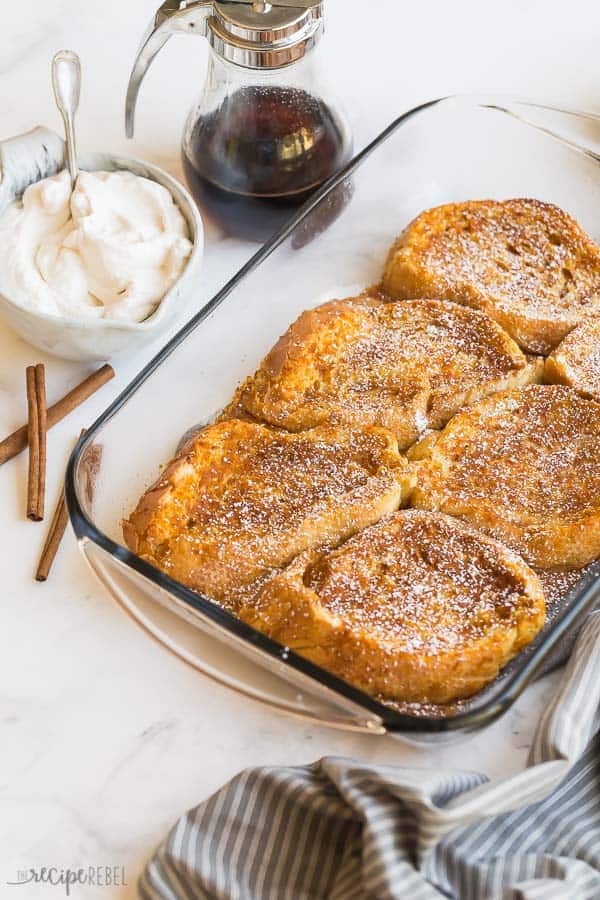 baked pumpkin french toast in glass baking dish with whipped cream syrup and cinnamon sticks