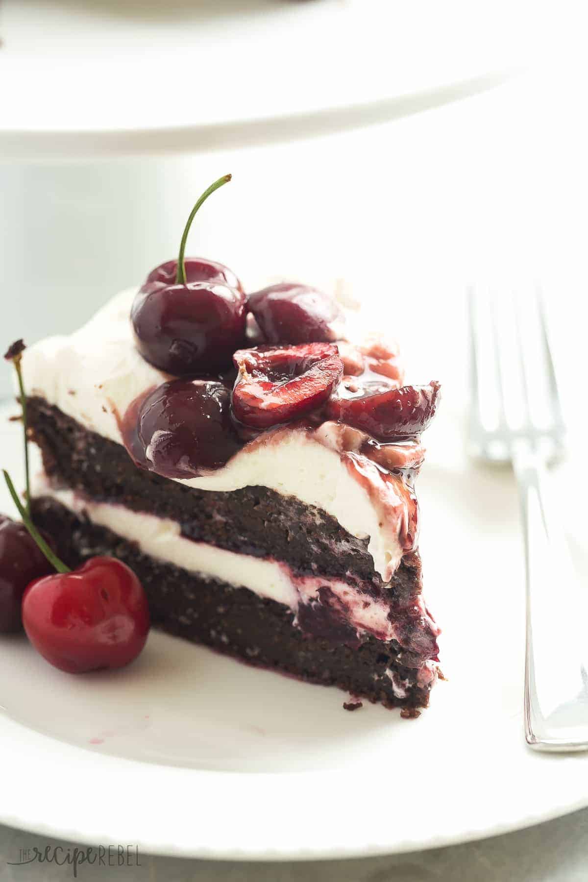 slice of gluten free black forest cake with two chocolate cake layers whipped cream and dark cherries