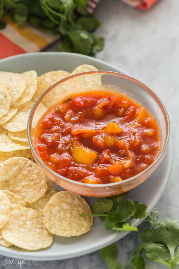 mango salsa in small glass bowl on grey plate with tortilla chips on the side
