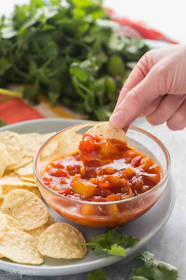 hand dipping chip in glass bowl with mango salsa