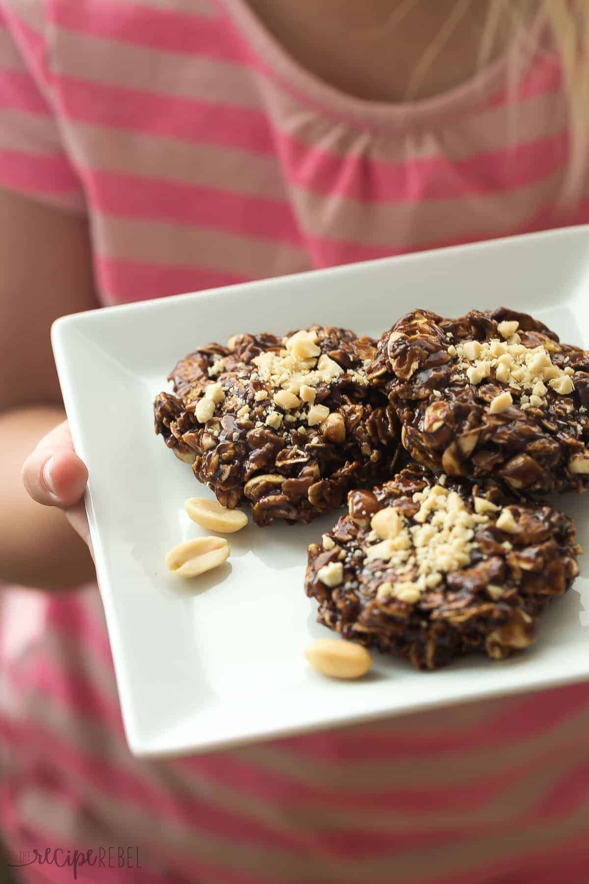 childs hands holding a plate of three no bake chocolate peanut butter cookies