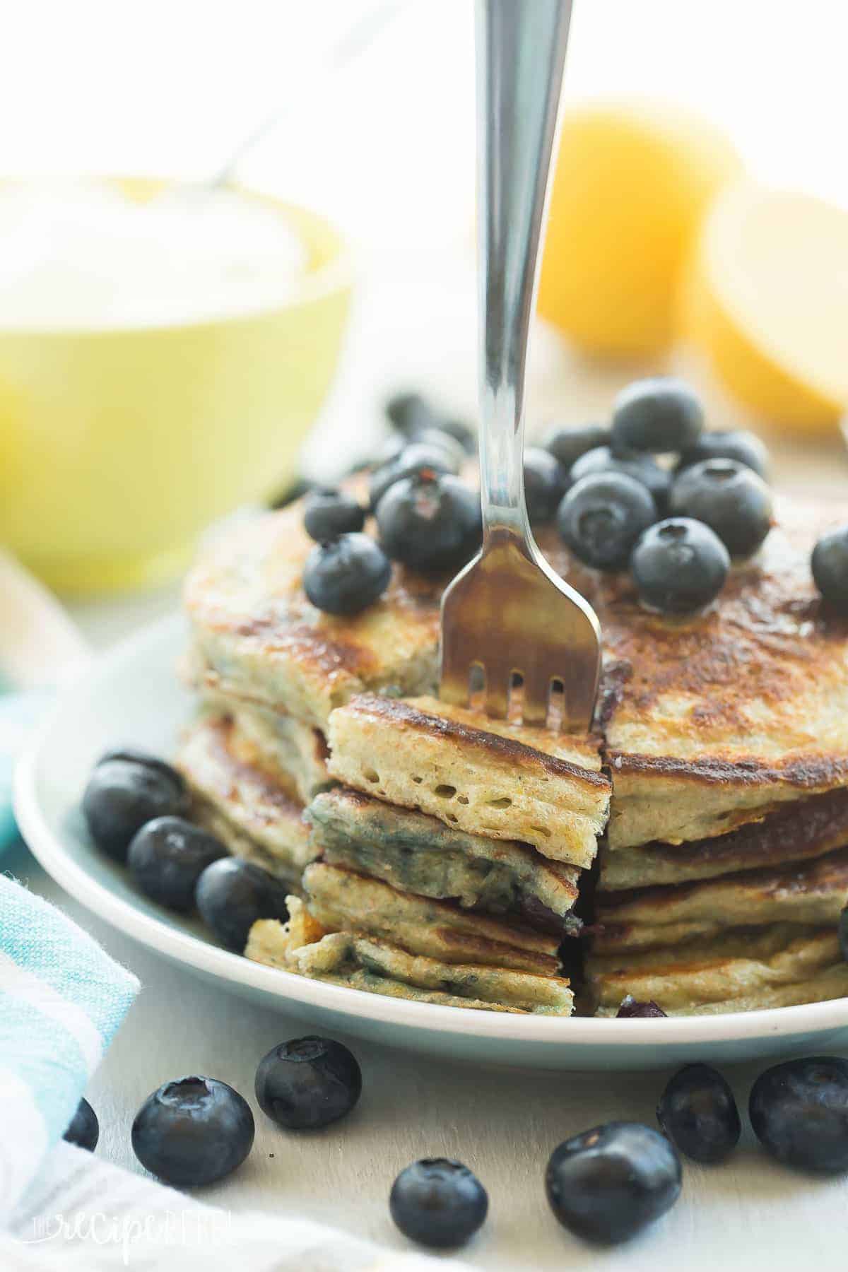 stack of lemon blueberry pancakes with fresh blueberries and fork taking a bite