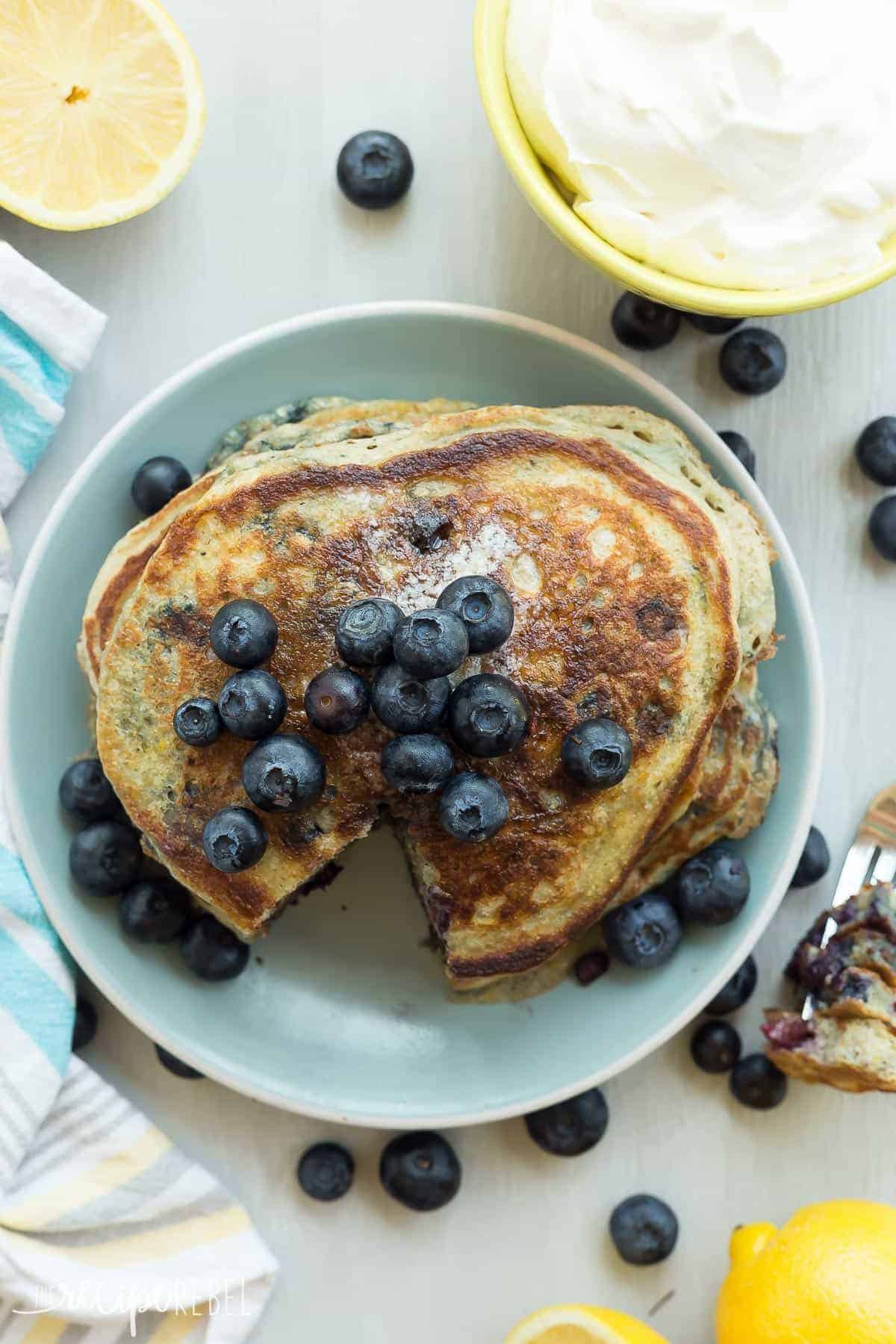 overhead image of lemon blueberry pancakes on plate with fresh blueberries and whipped cream on the side