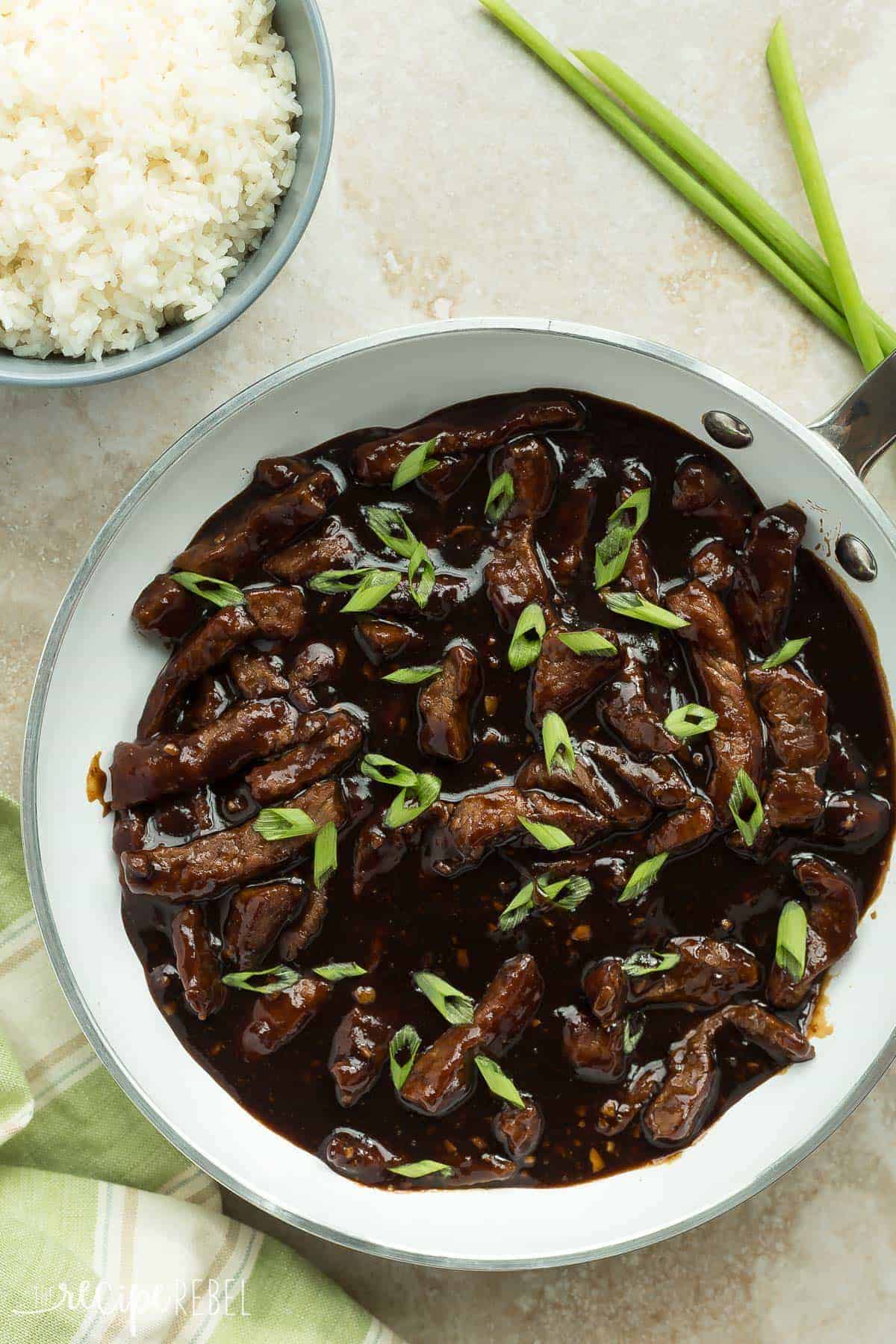 overhead image of maple ginger beef in white skillet with rice and green onions on the side