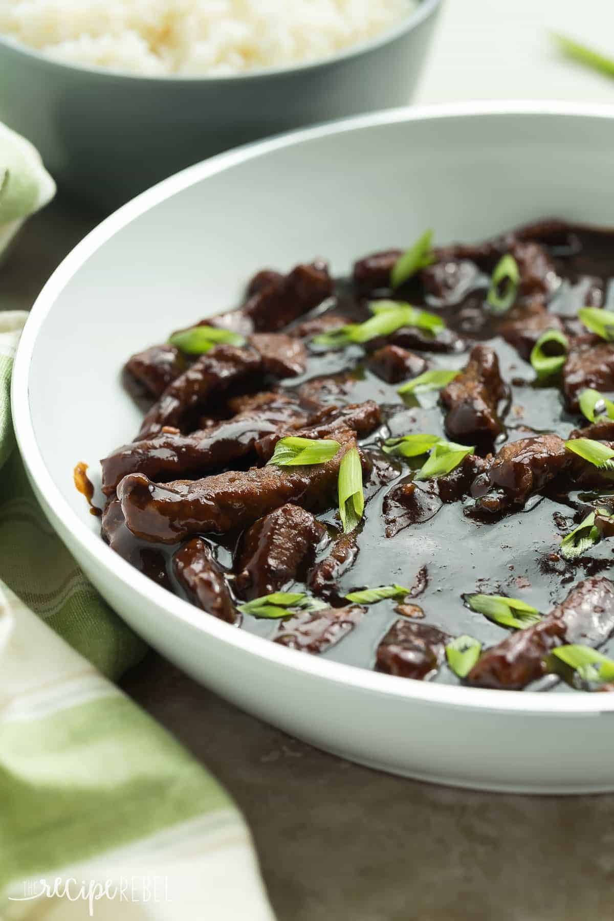 maple ginger beef in a white skillet topped with sliced green onion