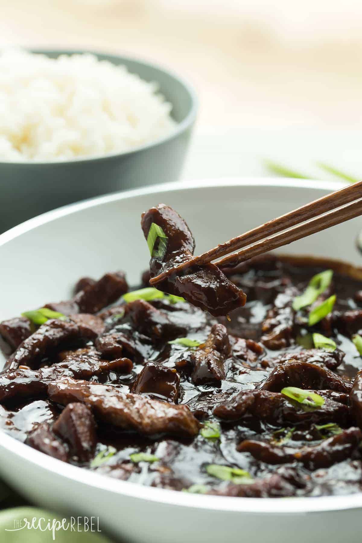 piece of maple ginger beef in chopsticks over pan of ginger beef