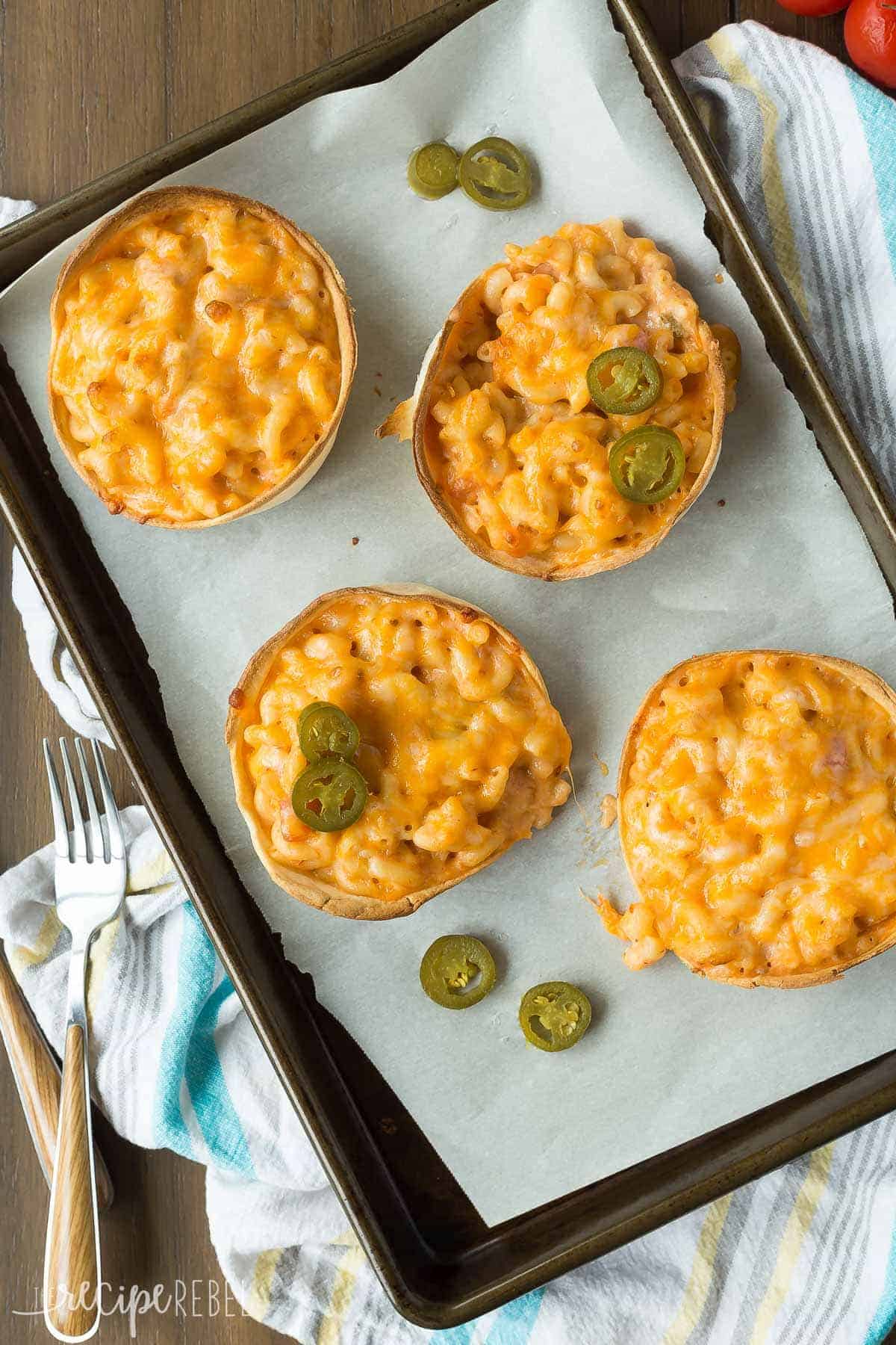overhead image of sheet pan with parchment paper topped with mexican mac and cheese in tortilla bowls