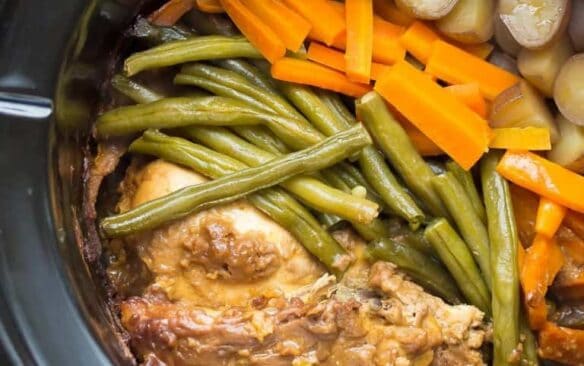 black crockpot with slow cooker peanut chicken and vegetables in it