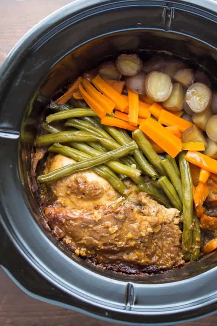 black crockpot with slow cooker peanut chicken and vegetables in it