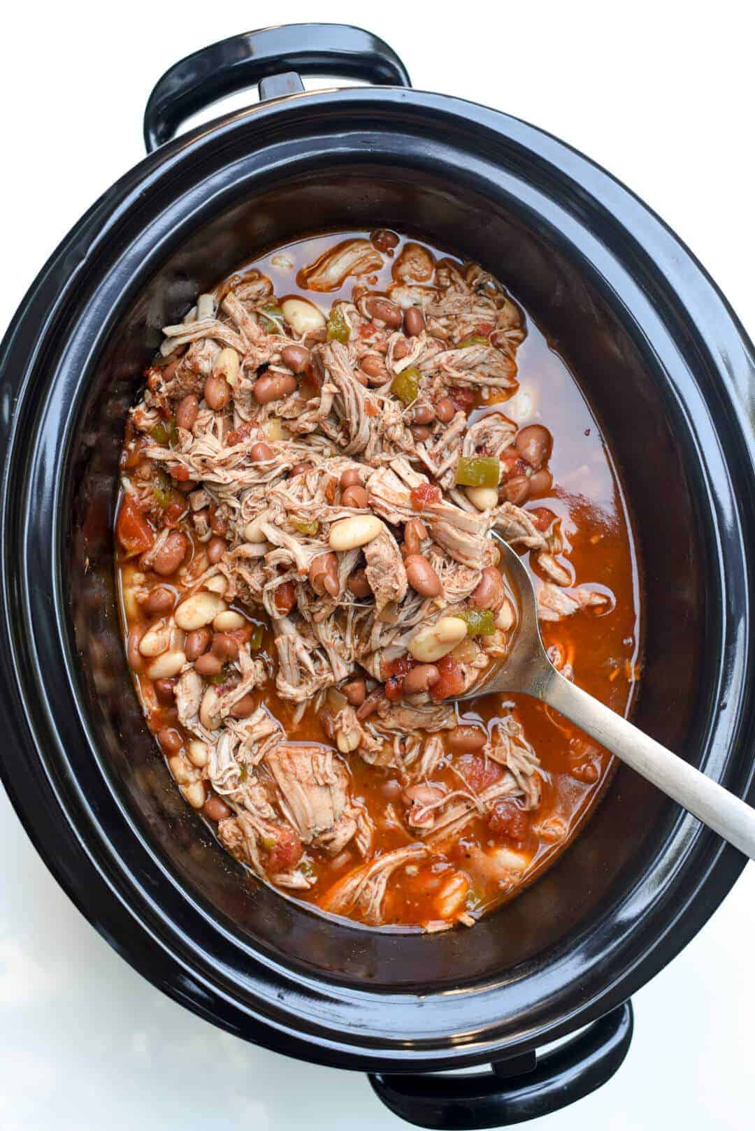 These Dump and Go Slow Cooker Recipes require no cooking or browning beforehand -- simply throw it in and walk away! Easy crock pot dump meals for busy weeknights and back to school! Chicken, beef, pork, or vegetarian -- there's something for everyone! #slowcooker #crockpot #dinner #recipes overhead image of black slow cooker with mexican pork and beans with metal spoon in pot