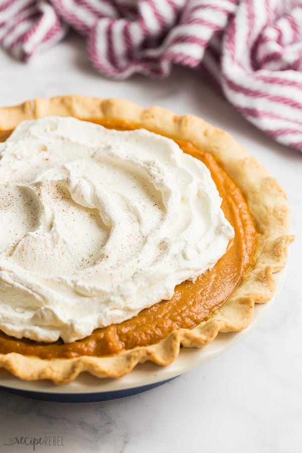 cream cheese pumpkin pie whole with whipped cream and purple towel in the background