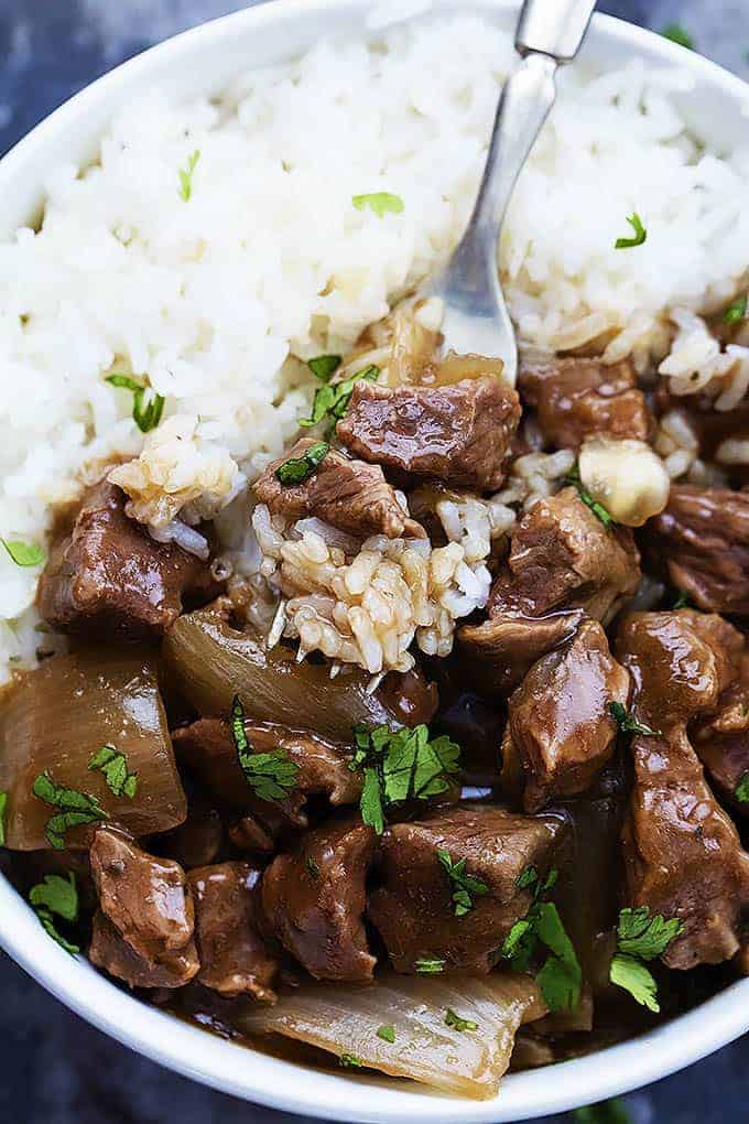 These Dump and Go Slow Cooker Recipes require no cooking or browning beforehand -- simply throw it in and walk away! Easy crock pot dump meals for busy weeknights and back to school! Chicken, beef, pork, or vegetarian -- there's something for everyone! #slowcooker #crockpot #dinner #recipes chunks of slow cooked beef and sauce over white rice with fork stuck in rice