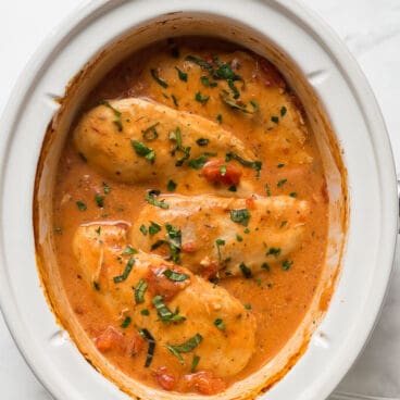 slow cooker creamy tomato basil chicken in a white crockpot