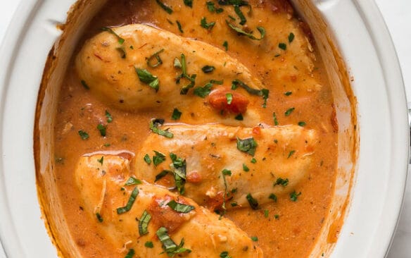 slow cooker creamy tomato basil chicken in a white crockpot