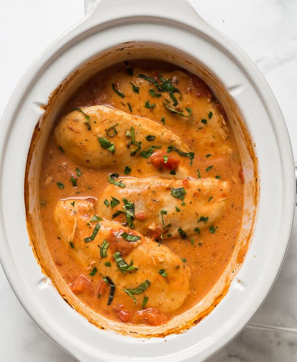 slow cooker creamy tomato basil chicken in a white crockpot
