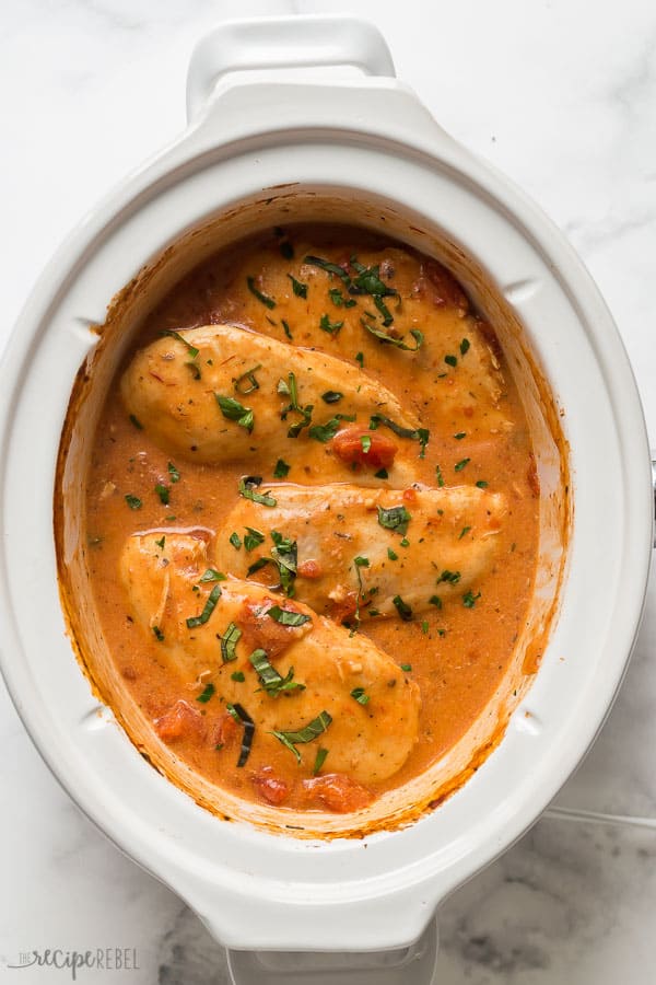 slow cooker creamy tomato basil chicken in a white crockpot