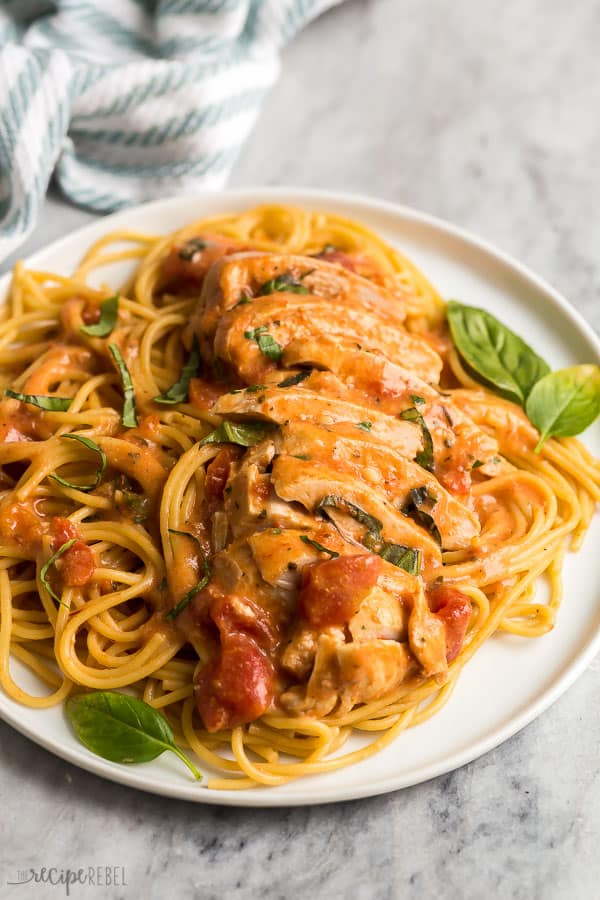 close up image of sliced tomato basil chicken breasts on plate of spaghetti