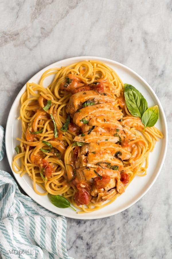 This Slow Cooker Creamy Tomato Basil Chicken is SO easy and flavorful, you wouldn't believe it only has just a few ingredients! The perfect easy dinner recipe for busy weeknights! #chicken #chickenbreast #slowcooker #crockpot #dinner overhead image of white plate with spaghetti and tomato basil chicken breast