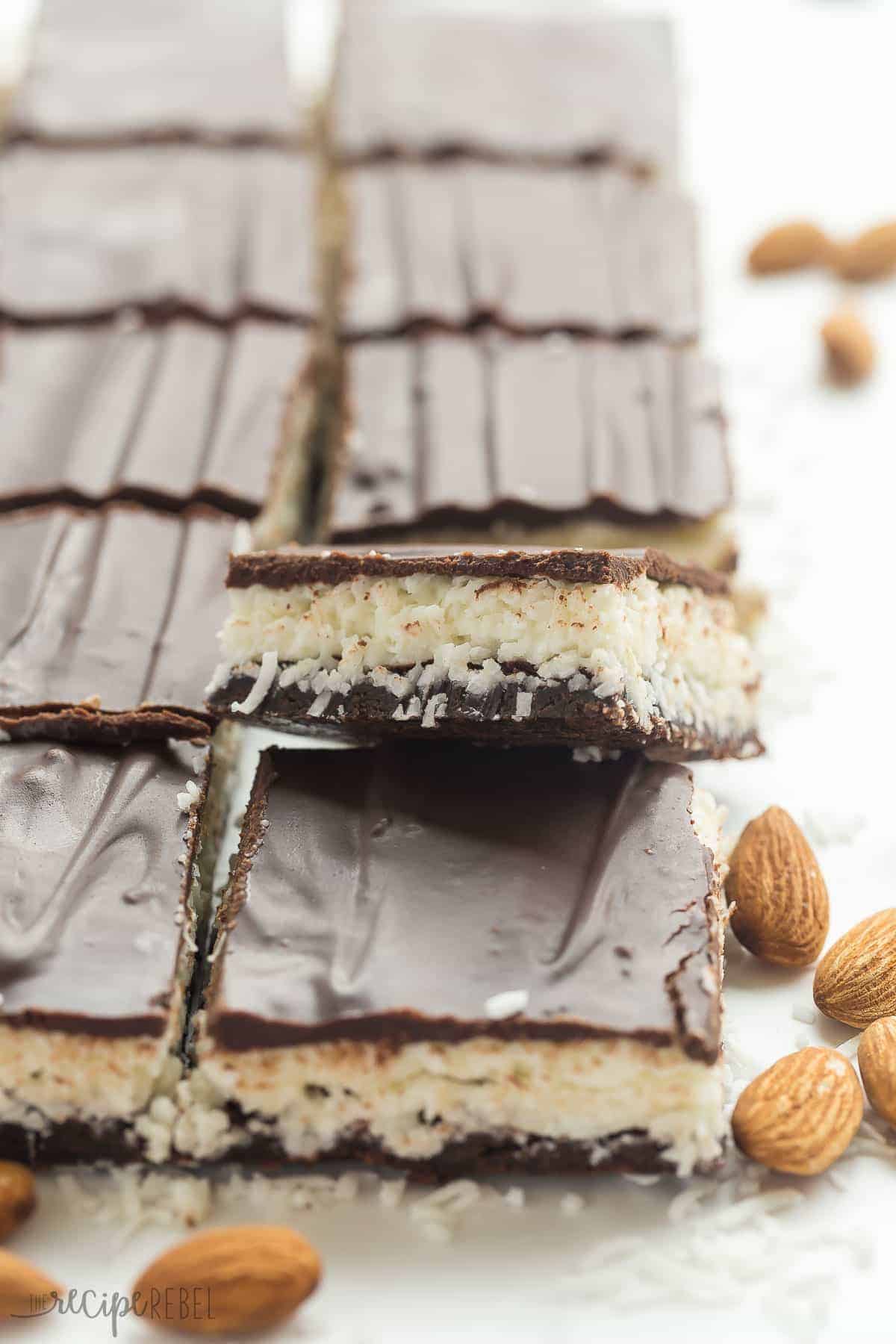 These Almond Joy Brownies have a thin, fudgy brownie layer and are topped with a creamy coconut filling, almonds and a layer of chocolate! They are an easy treat for the holidays! full pan of almond joy brownies cut into squares on parchment paper with one square sticking up