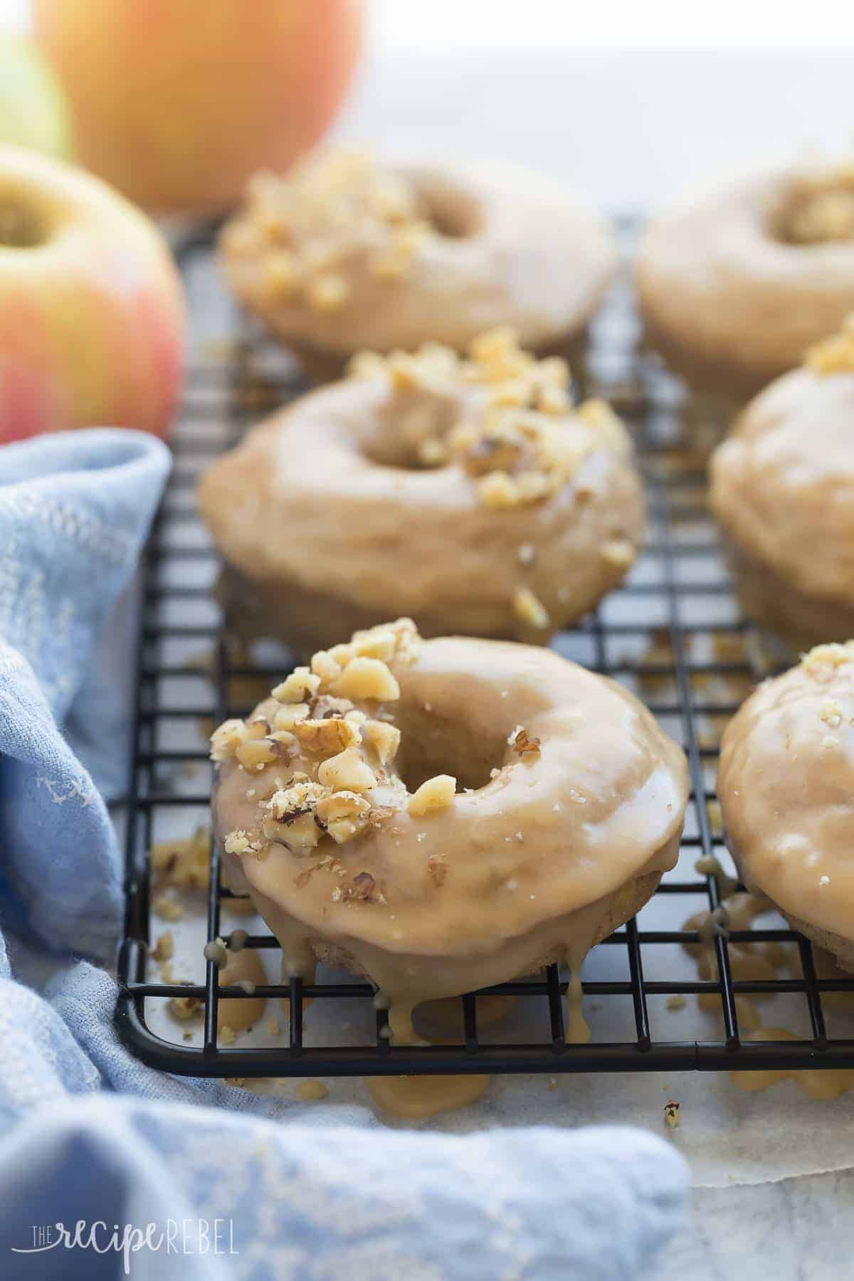 apple cinnamon baked donuts lined up on black cooling rack with glaze and chopped pecans