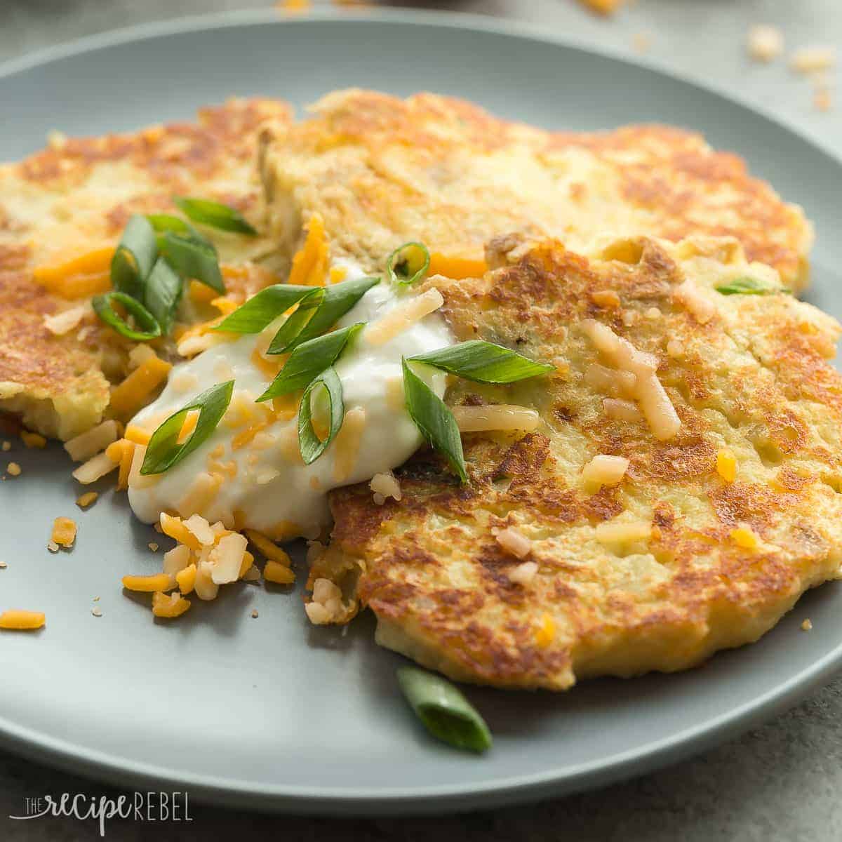 close up image of mashed potato pancakes on grey plate with sour cream and green onions