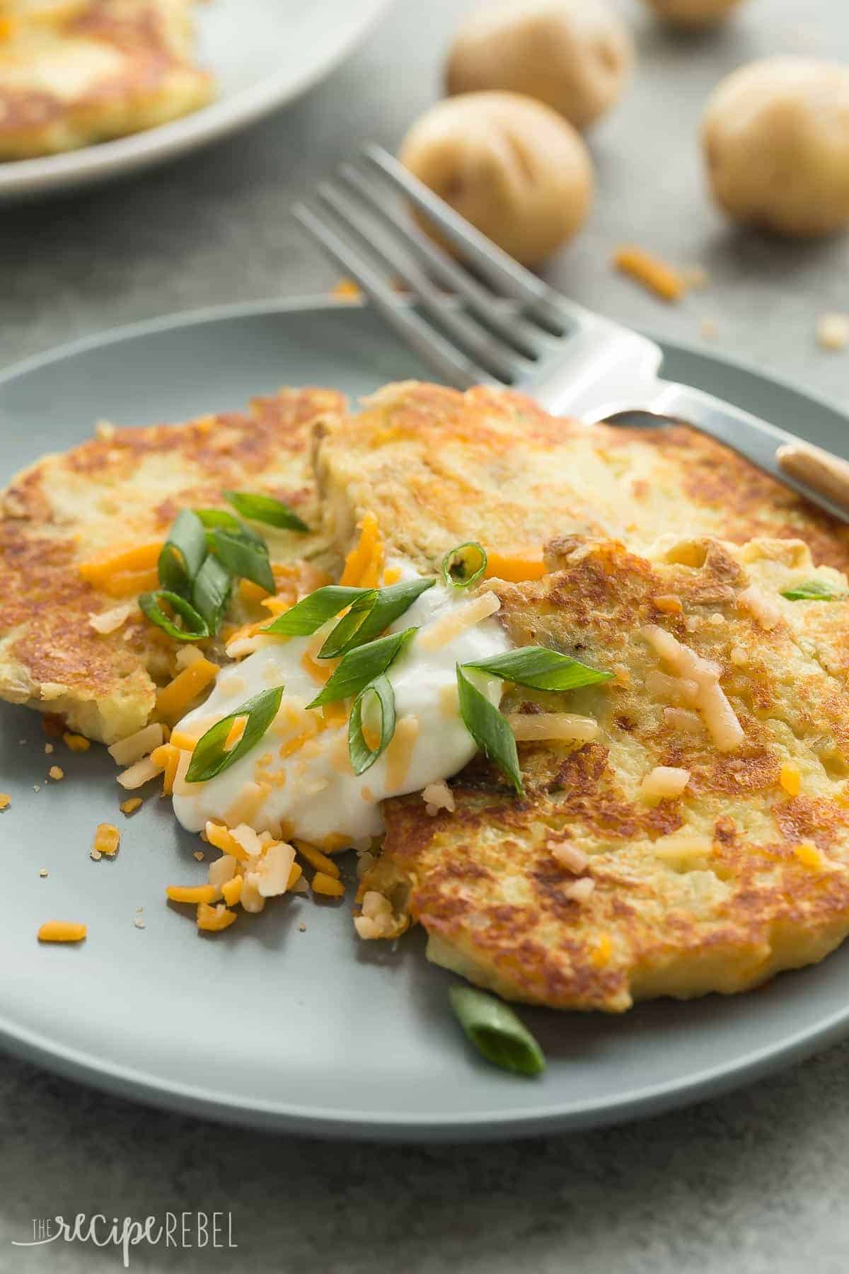 close up image of mashed potato pancakes on grey plate with sour cream green onions and cheddar cheese