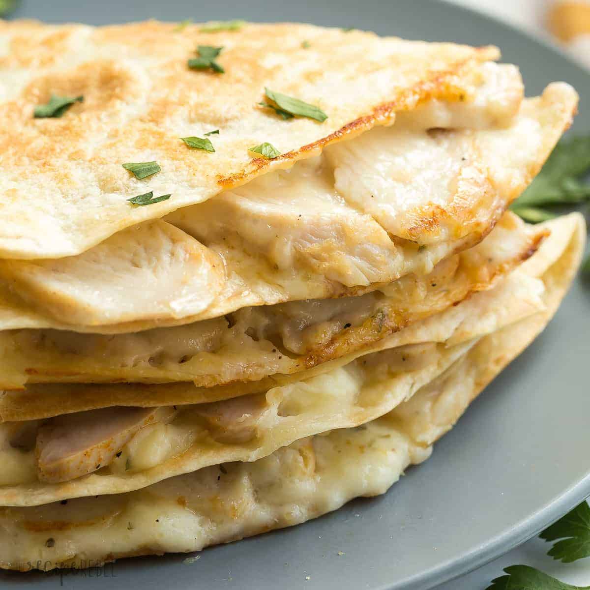 close up image of chicken alfredo quesadillas stacked on grey plate