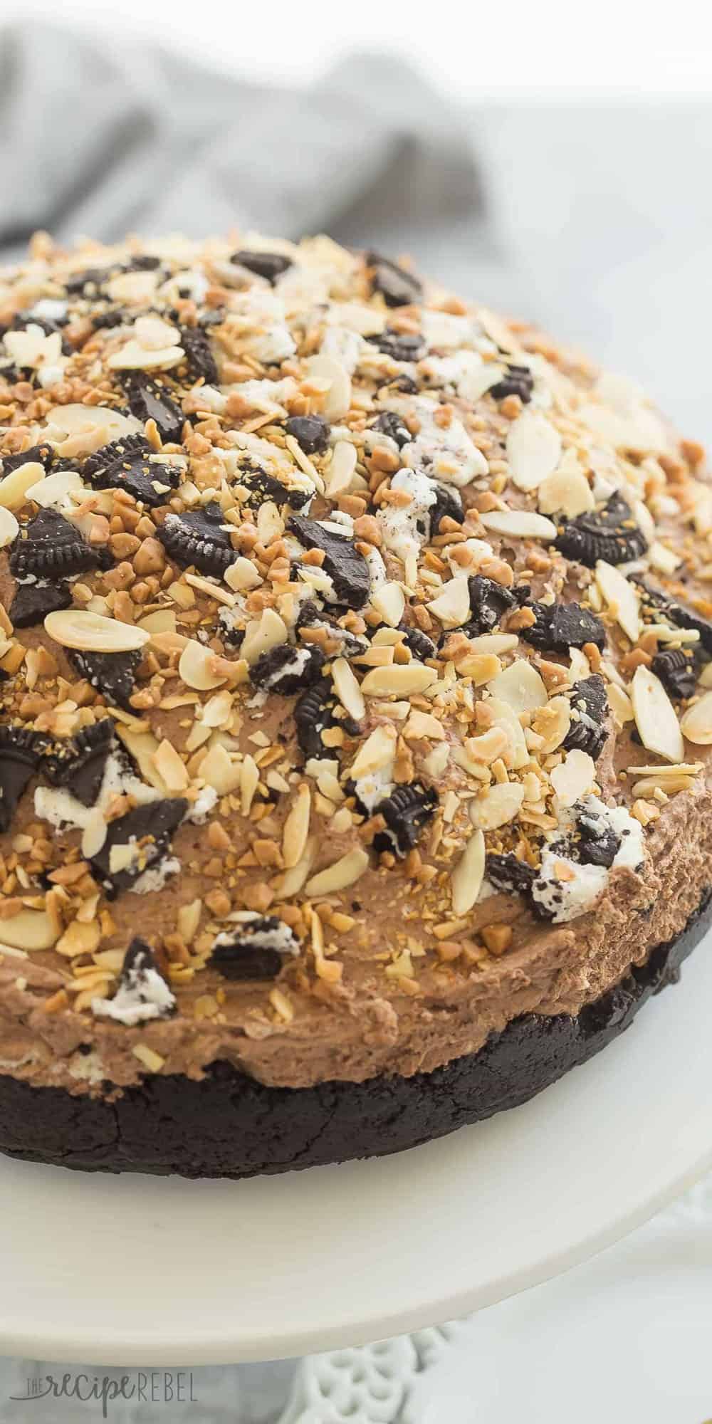 Sometimes you just need a mountain of chocolate! This Chocolate Explosion has rich chocolate mousse piled high on an Oreo crust, filled with chunks of vanilla cheesecake, Oreos, nuts, toffee bits -- truly indulgent! tall image of whole chocolate explosion topped with almonds crushed oreos and toffee bits
