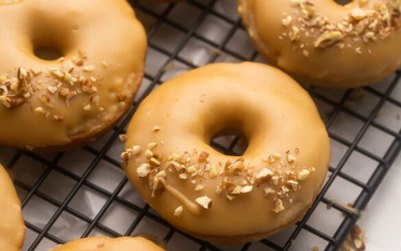 square image of apple donuts on baking rack with glaze.