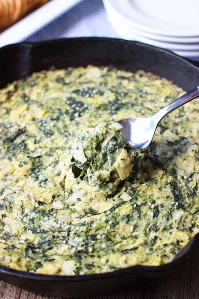 spinach artichoke dip in black skillet with spoon scooping some