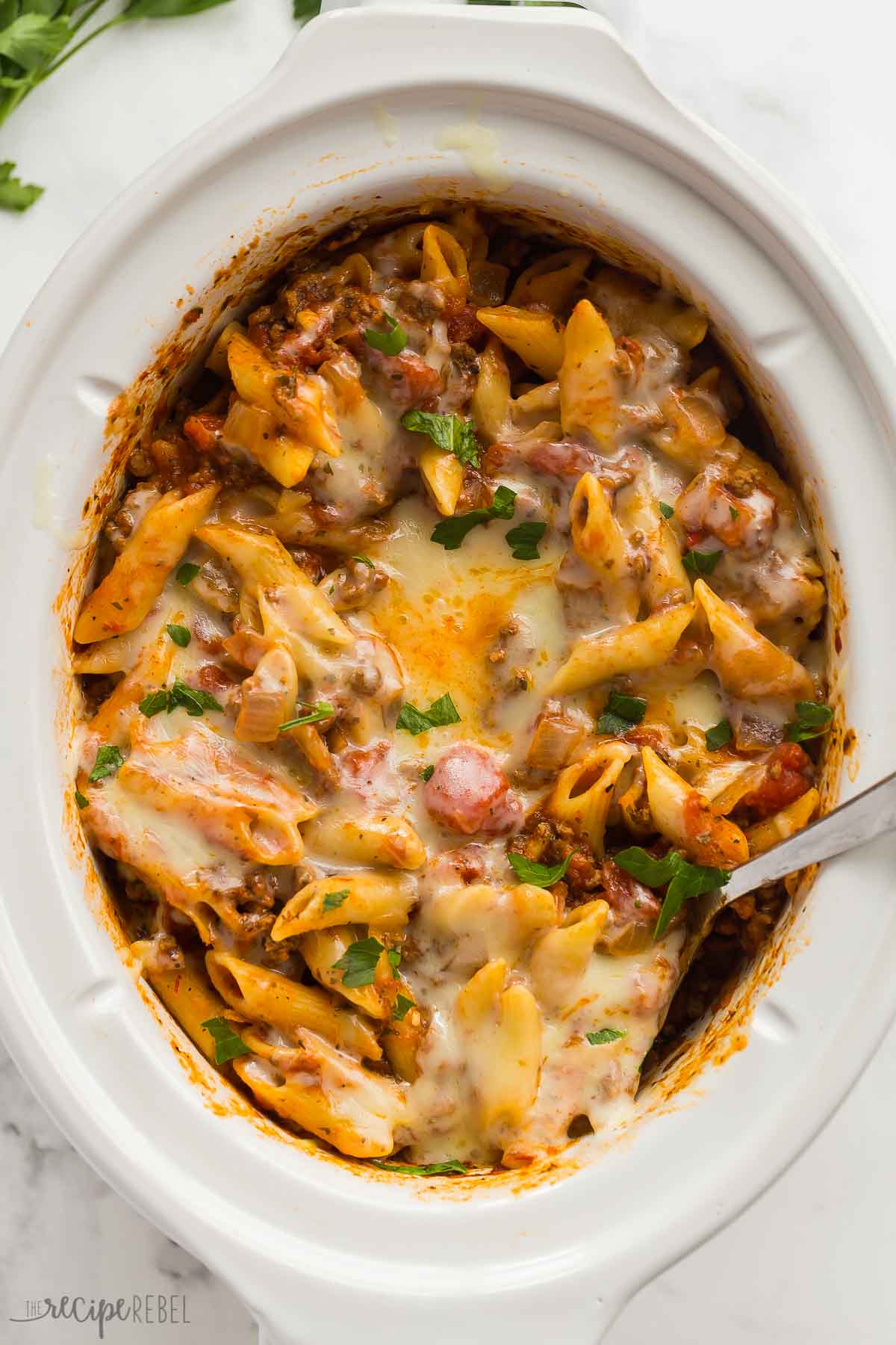 overhead image of slow cooker baked ziti in white crockpot.