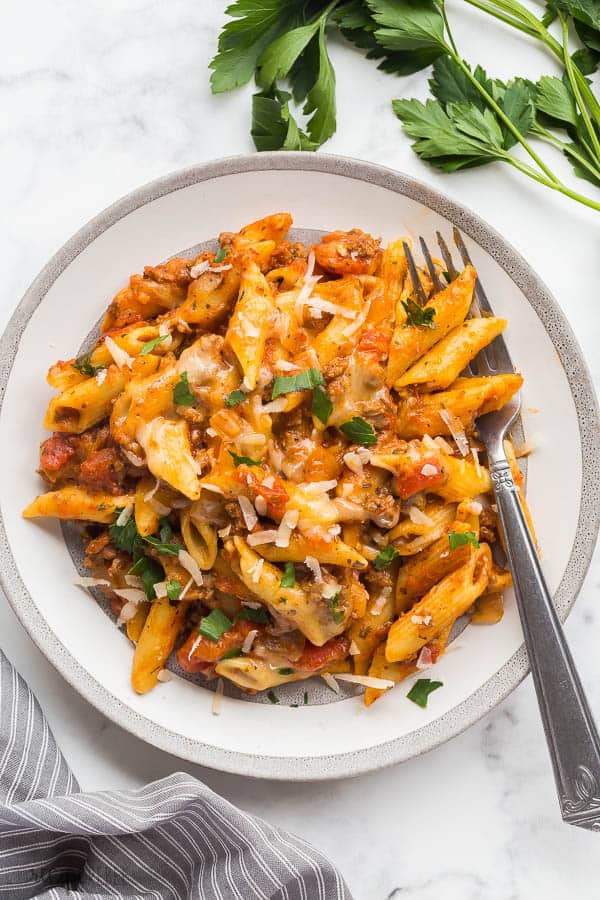 crock pot baked ziti on grey plate with fork stuck into pasta on white marble background