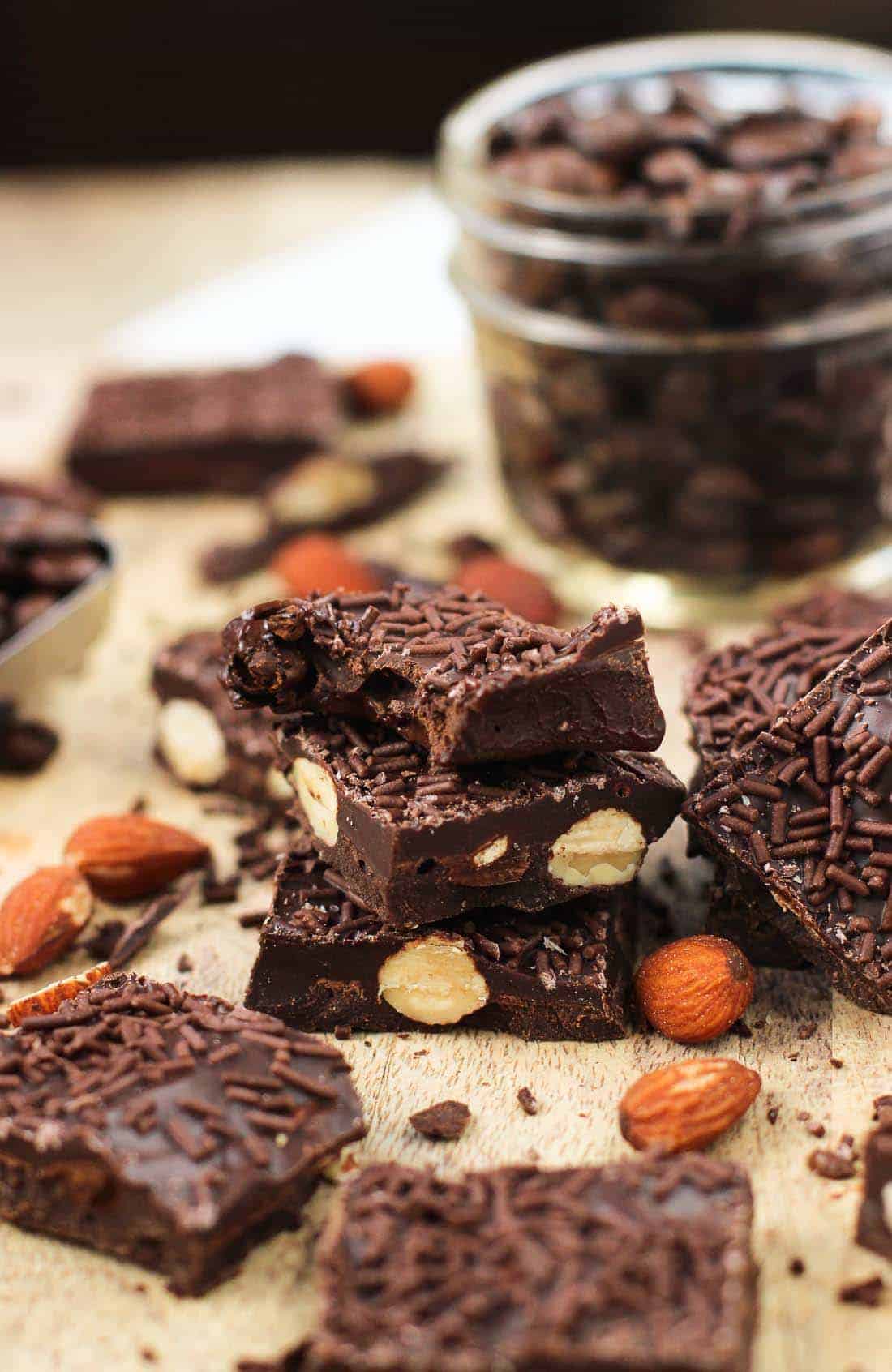 chocolate covered espresso bean bark with almonds stacked and whole almonds around it